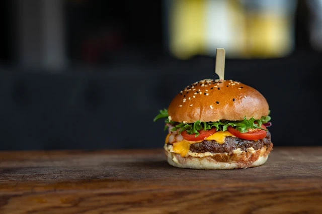 Burger présenté sur une planche en bois, fond flouté